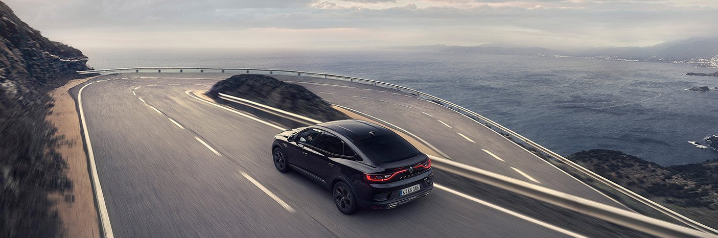Schwarzes Auto fährt auf einer kurvenreichen Küstenstraße mit Blick auf das Meer.