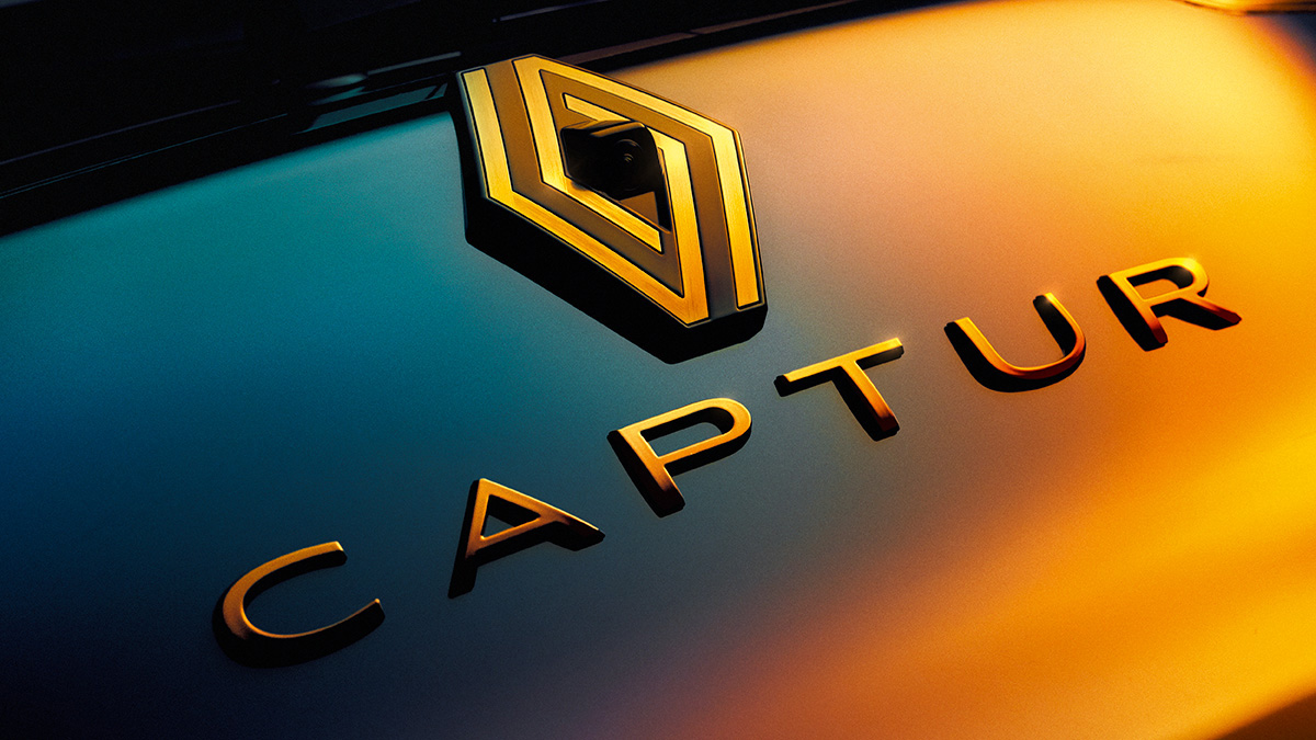 Nahaufnahme des Renault Captur-Logos in goldenen Buchstaben auf einem dunklen, reflektierenden Hintergrund.