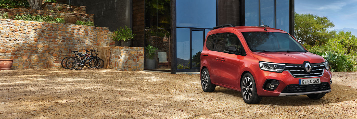 Ein rotes Renault Auto parkt vor einem modernen Glasgebäude, umgeben von Natur und Fahrrädern.