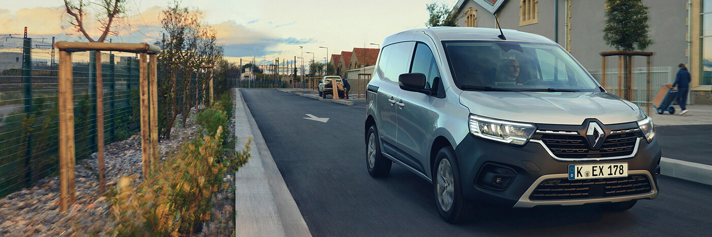 Silberner Renault fährt auf einer modernen Straße mit Bäumen und Häusern im Hintergrund.