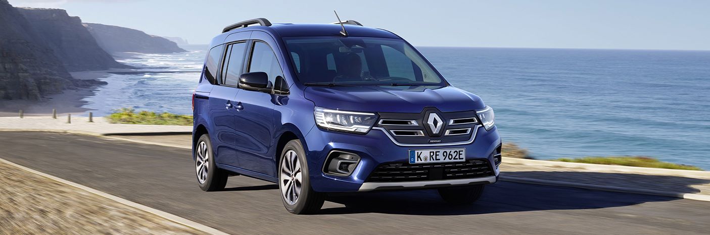 Blauer Renault-Minivan fährt entlang der Küste bei klarem Himmel und Meer im Hintergrund.
