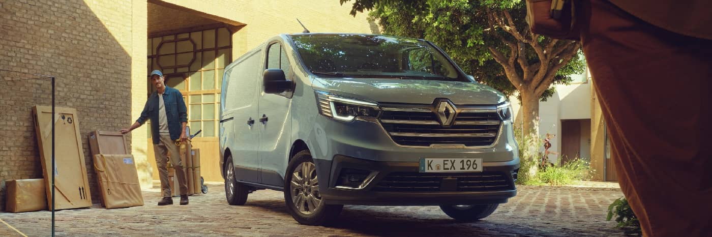Ein Renault Lieferwagen parkt in einer urbanen Umgebung, während ein Mann Lieferkartons bewegt.
