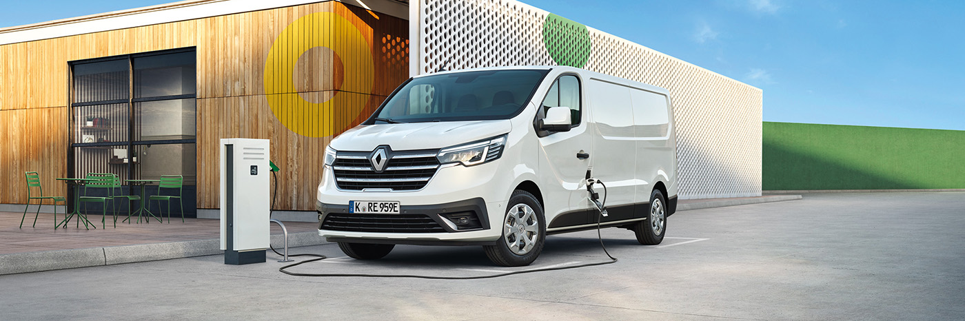 Ein weißer Elektrotransporter von Renault steht an einer Ladestation auf einem Parkplatz.