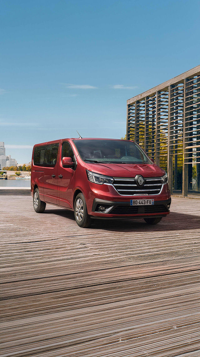 Roter Renault Van vor einer modernen Stadtlandschaft am Wasser, mit Holzsteg im Vordergrund.
