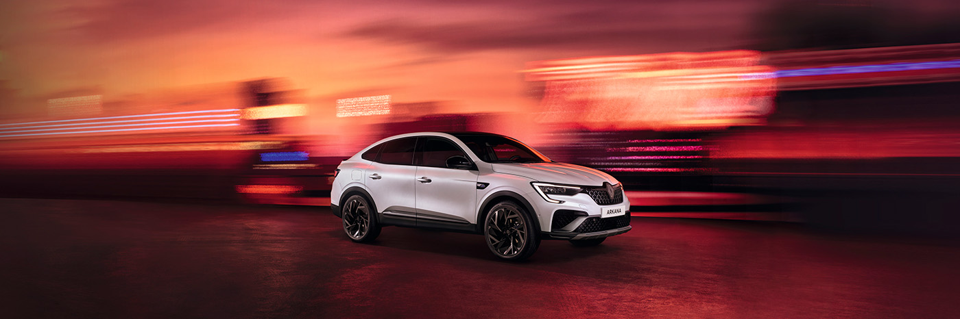 Ein weißer SUV im Fahrmodus vor einem verschwommenen, bunten Hintergrund bei Sonnenuntergang.