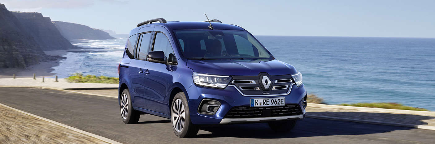 Blauer Renault Kastenwagen auf einer Küstenstraße mit Meerblick im Hintergrund.