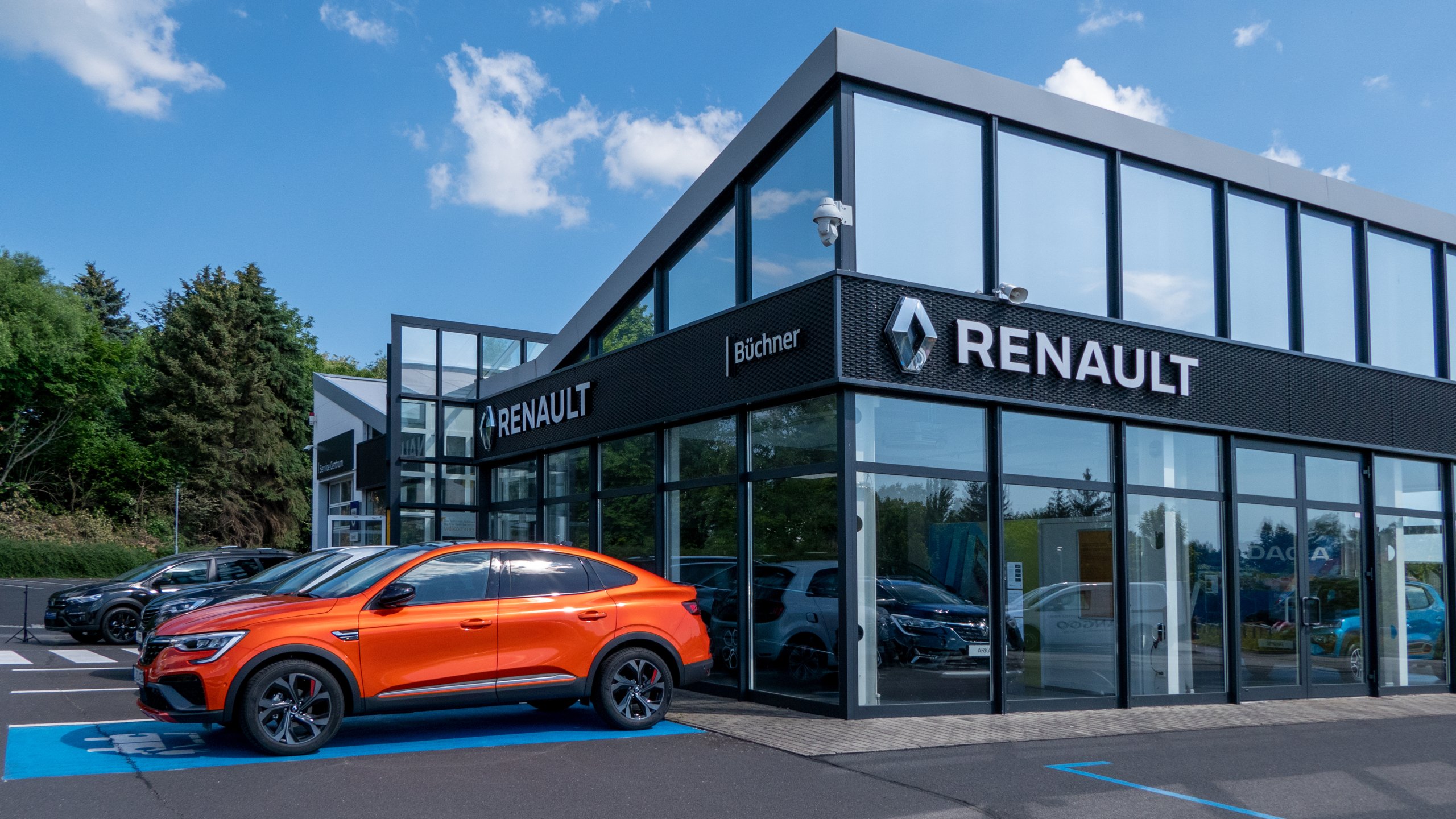 Renault Autohaus mit orangefarbenem Fahrzeug und modernen Glasfassaden unter blauem Himmel.