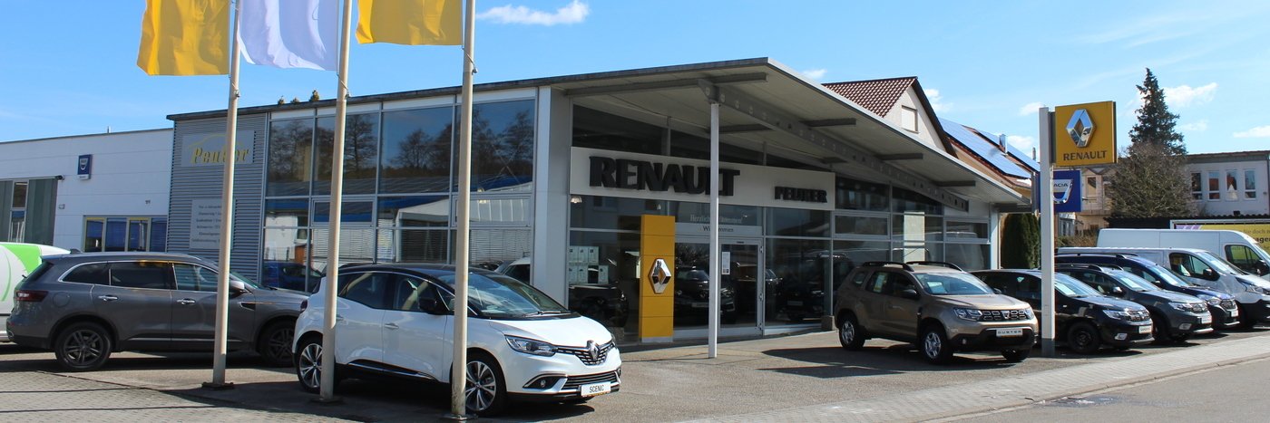 Renault Autohaus mit mehreren Fahrzeugen vor dem Gebäude und Fahnen, sonniger Tag.