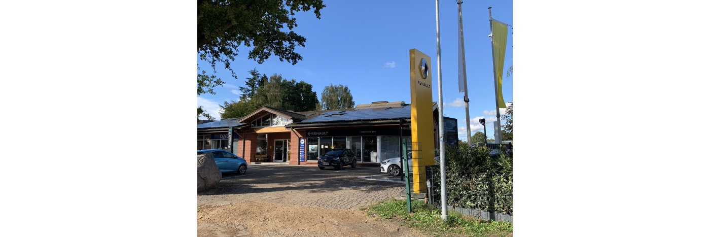 Renault Autohaus mit moderner Fassade, Solarzellen und Ausstellungsautos im Freien, umgeben von grüner Landschaft.