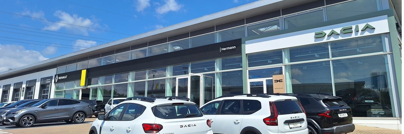 Dacia-Autohaus mit verschiedenen Fahrzeugen vor dem Gebäude und klarem blauen Himmel.