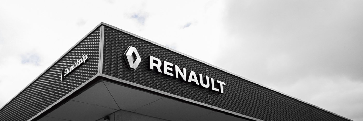 Das Renault Logo an der Fassade eines modernen Autohauses unter einem bewölkten Himmel.