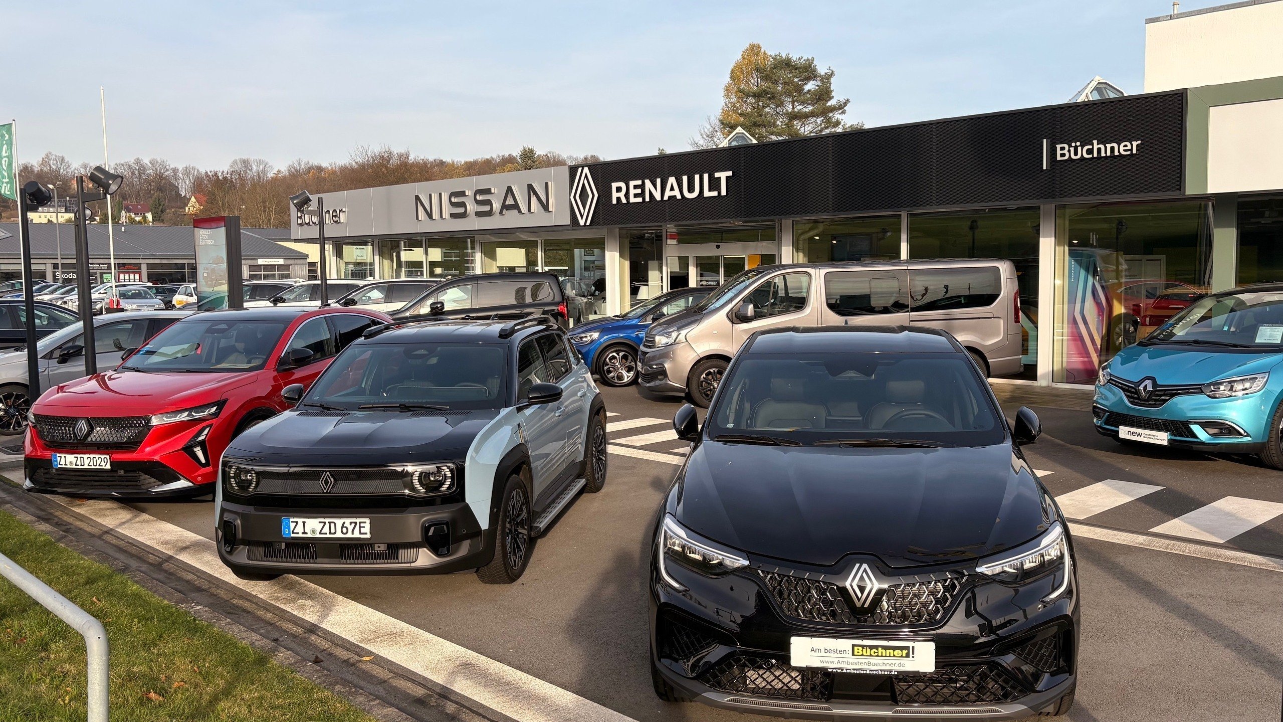 Autos und Fahrzeugmodelle vor dem Nissan Renault Autohaus Büchner, mit mehreren Fahrzeugen in verschiedenen Farben.