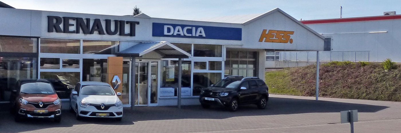 Das Autohaus von Renault und Dacia mit mehreren Fahrzeugen vor dem Eingang in einem sonnigen Neubaugebiet.