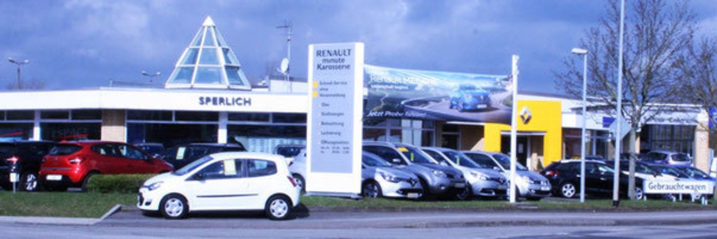 Renault Autohaus mit verschiedenen Fahrzeugen und Kundenparkplätzen, klarer Himmel im Hintergrund.