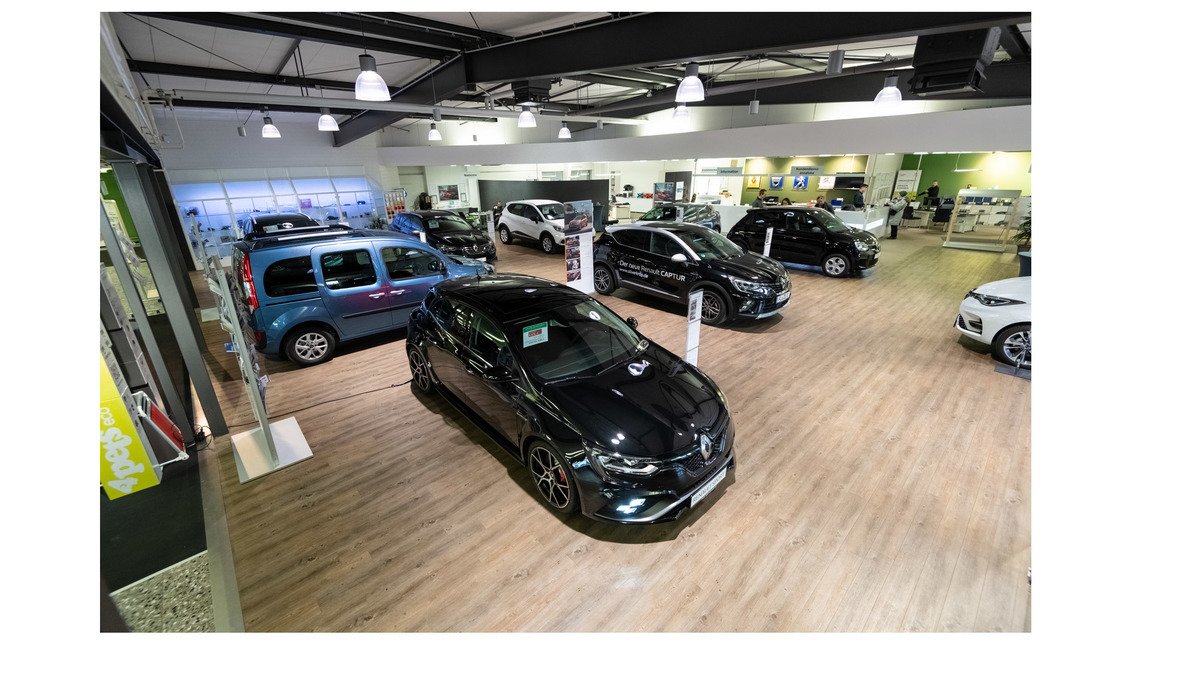 Autohaus mit mehreren Fahrzeugen, darunter ein schwarzes Renault-Modell und ein blauer Kompaktwagen auf Holzfußboden.