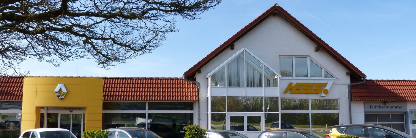 Renault- und Autohändler HESS in ländlicher Umgebung, moderne Architektur und klare Sicht. Fahrzeugparkplatz im Vordergrund.