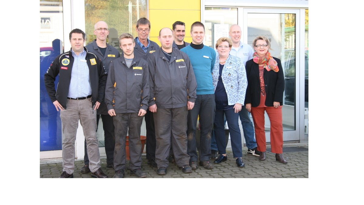 Gruppe von 11 Personen, die vor einem Gebäude stehen, in Arbeitskleidung und Freizeitkleidung, mit freundlichen Gesichtern.
