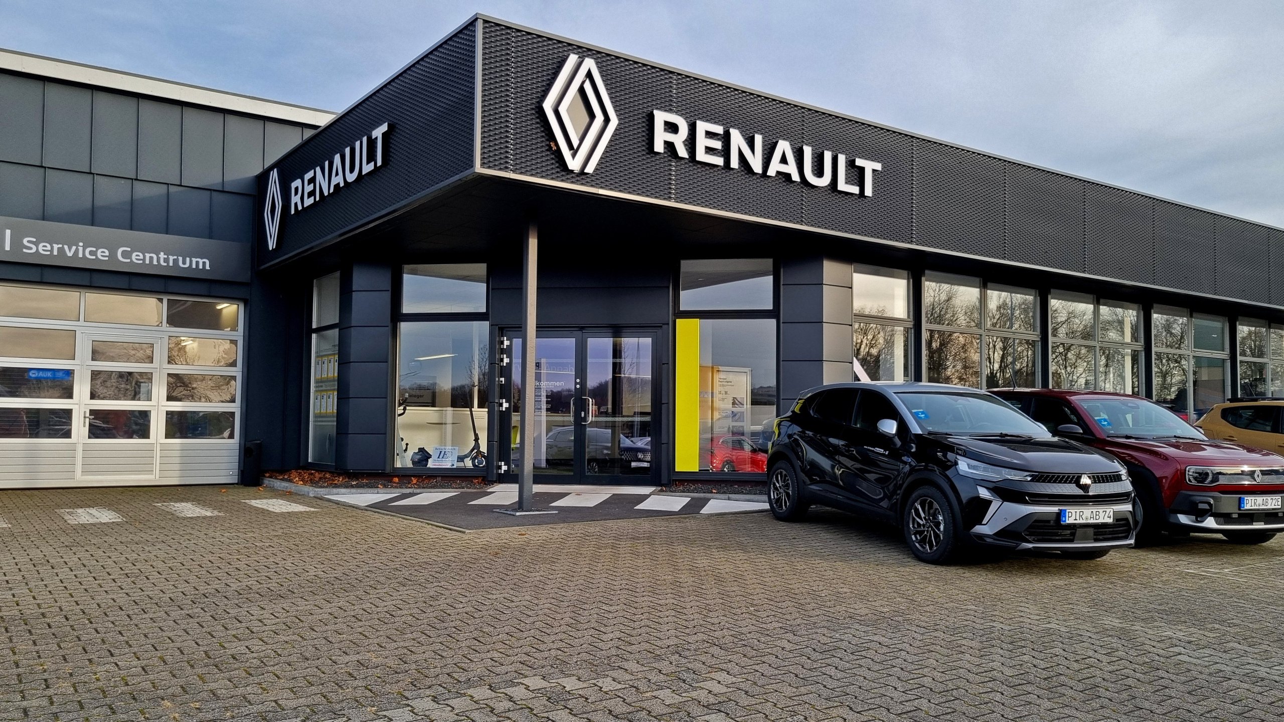 Renault Autohaus mit modernem Design und mehreren Fahrzeugen auf dem Parkplatz, sonniger Tag.