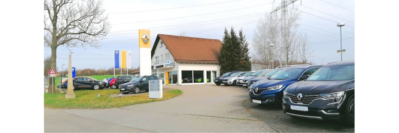 Renault Autohaus mit mehreren Autos auf dem Parkplatz und einem Gebäude im Hintergrund.