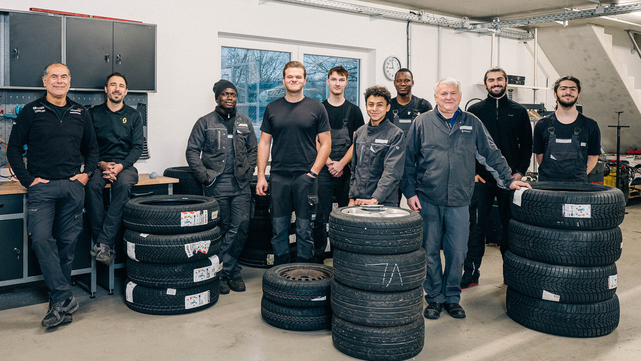 Ein Team von Technikern steht in einer Werkstatt mit Reifen, umgeben von Werkzeug und Ausrüstung.