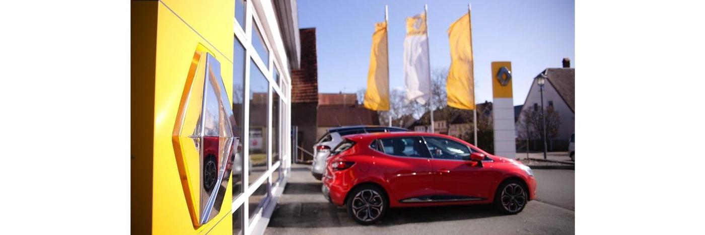 Rotes Auto vor einem Renault Autohaus mit gelbem Logo und Fahnen im Hintergrund.