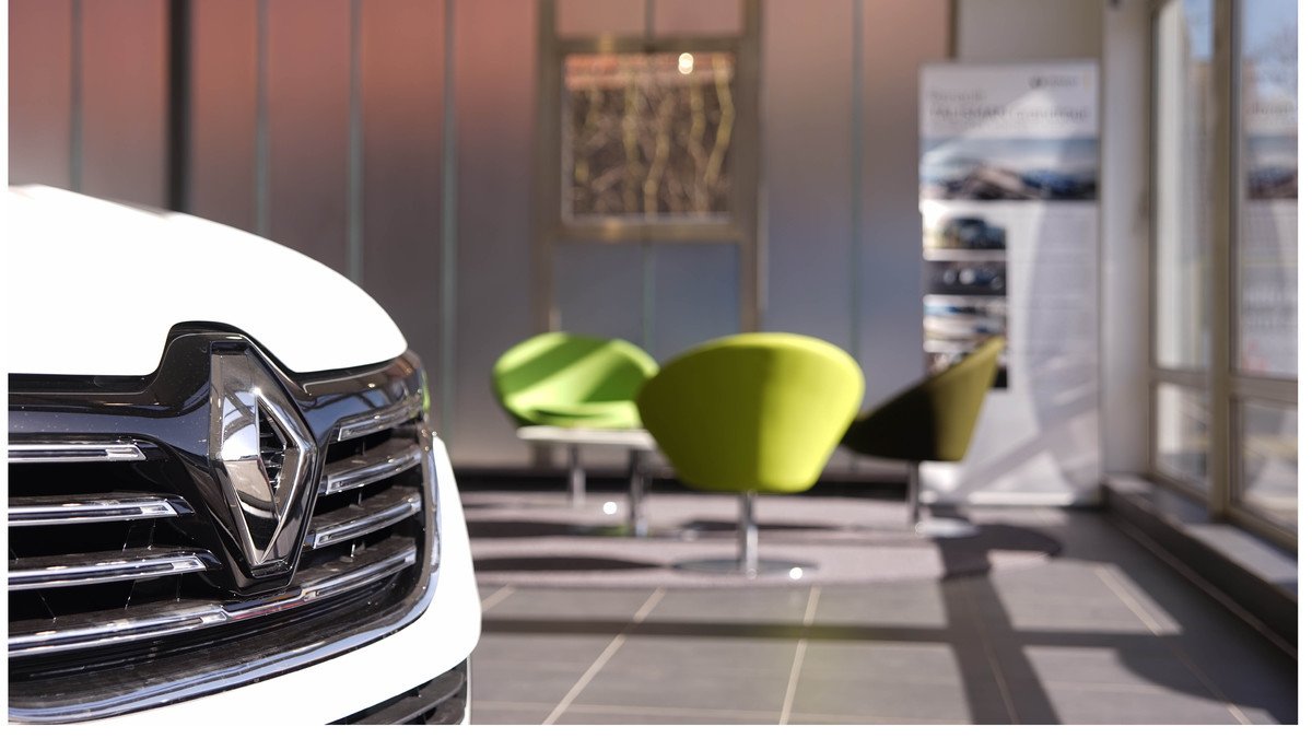 Nahaufnahme des Renault-Emblems in einem modernen Showroom mit leuchtend grünen Stühlen im Hintergrund.