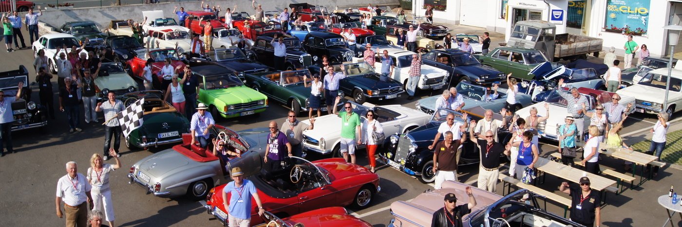Große Ansammlung von klassischen Autos und Menschen auf einem Parkplatz bei einer Autoausstellung.