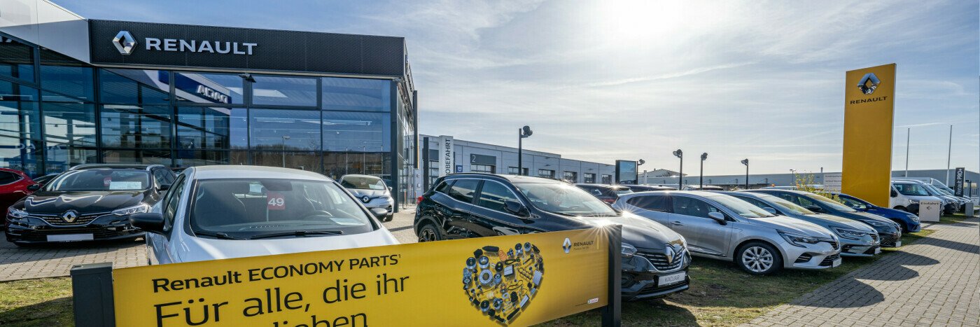 Renault Autohaus mit einer Reihe von Fahrzeugen und einem gelben Werbeschild im Vordergrund.