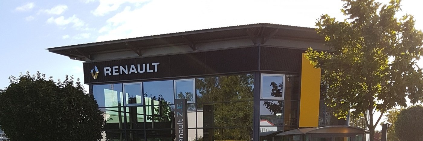 Renault-Gebäude mit Glasfassade und gelbem Akzent, umgeben von Bäumen und klarem Himmel.