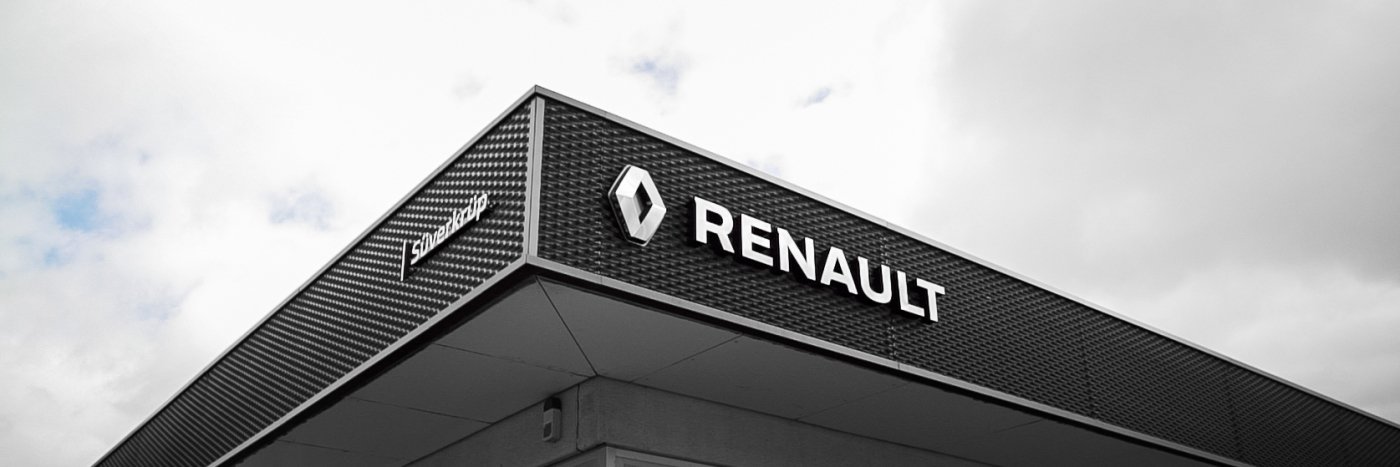 Das Renault Logo an einer modernen Autowerkstatt unter einem bewölkten Himmel.