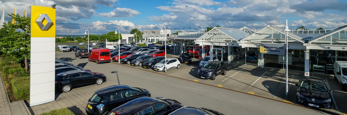 Renault Autohaus mit vielen Fahrzeugen auf dem Parkplatz, unter blauem Himmel und Wolken.