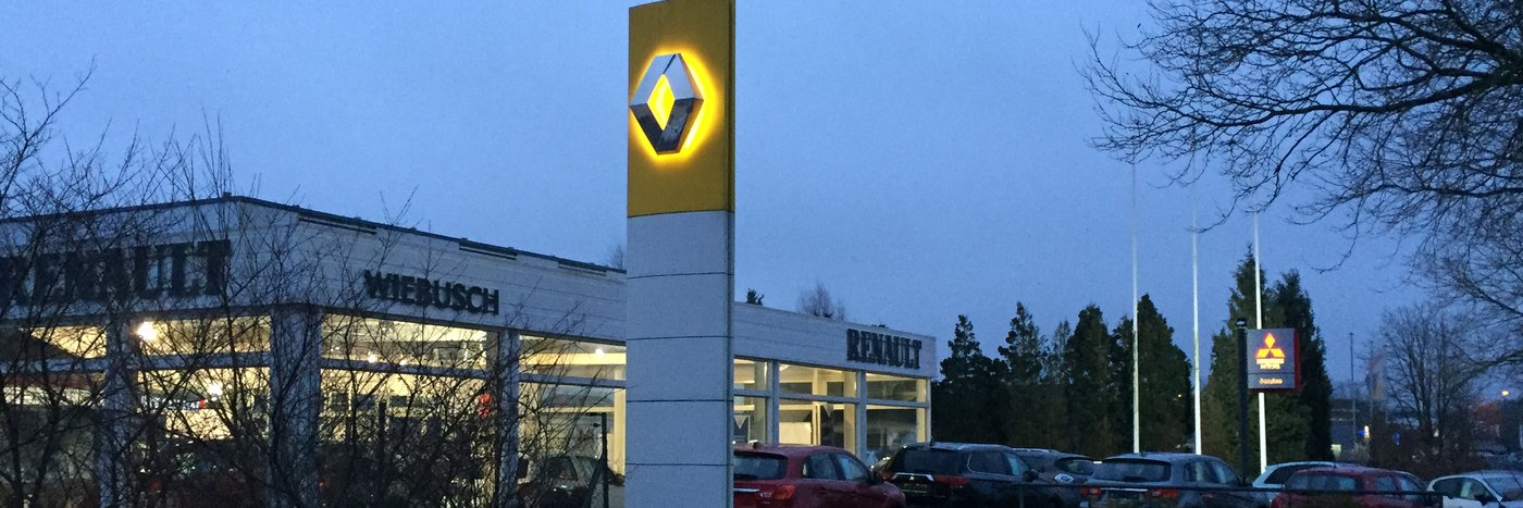 Renault Autohaus bei Dämmerung mit leuchtendem Logo und Fahrzeugen auf dem Parkplatz.