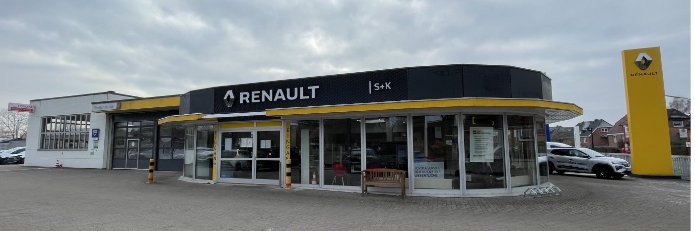 Renault Autohaus mit moderner Fassade, gelbem Dach und ausgestellten Autos auf dem Parkplatz, unter grauem Himmel.