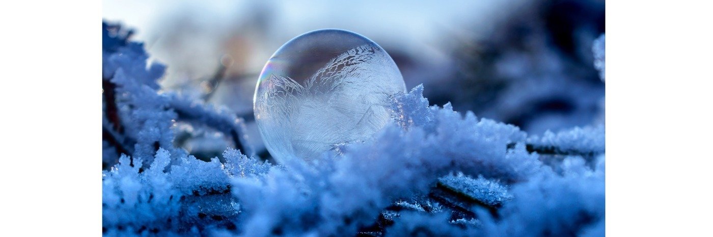 Eine gefrorene Blase auf frostigem Gras mit filigranen Mustern im Eis, in einer kühlen blauen Farbpalette.