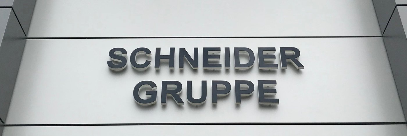 Schild mit dem Schriftzug 'SCHNEIDER GRUPPE' an einer modernen Gebäudeausstattung.