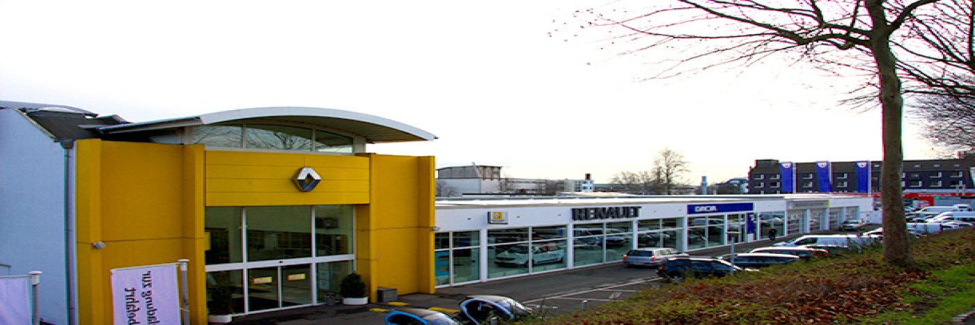 Renault Autohaus mit gelber Fassade und ausgestellten Fahrzeugen, umgeben von Parkplätzen und Bäumen.