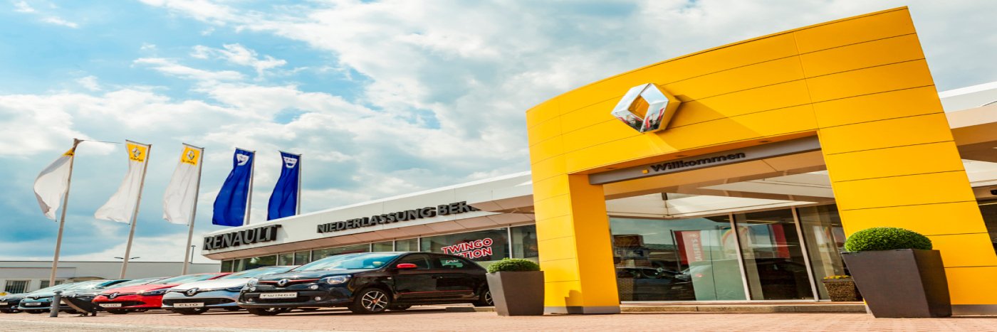 Renault Autohaus mit gelbem Eingang, Flaggen und Autos auf dem Parkplatz, unter blauem Himmel.