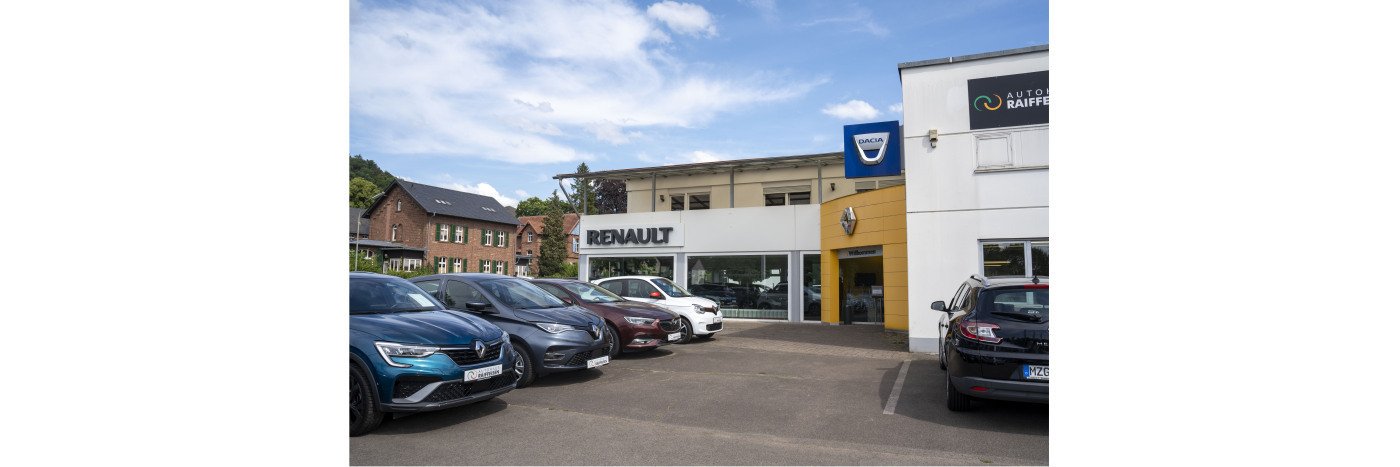Renault Autohaus mit mehreren Fahrzeugen auf dem Parkplatz und blauem Himmel im Hintergrund.