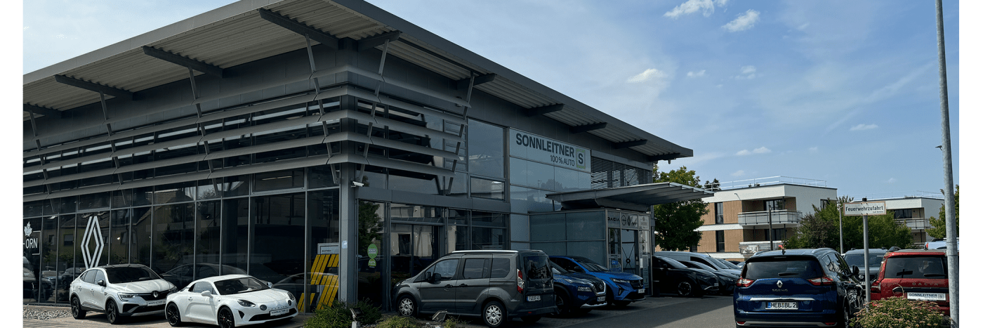 Das Autohaus Sonnleitner mit mehreren Autos auf dem Parkplatz und modernem Gebäude im Hintergrund.