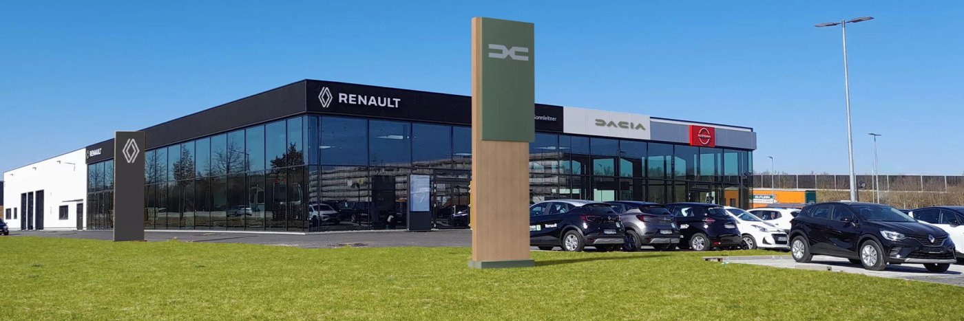 Autohäuser von Renault und Dacia, moderne Architektur mit Glasfassade und ausgestellten Autos auf der Wiese.