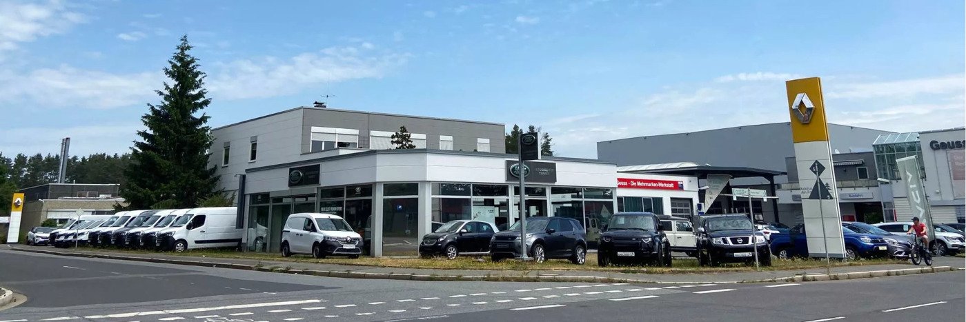 Autohaus mit verschiedenen Fahrzeugen und einem Renault-Schild, umgeben von Bäumen und Parkplätzen.