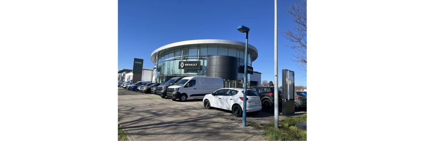 Renault Autohaus mit mehreren Fahrzeugen auf dem Parkplatz und klarem blauen Himmel.