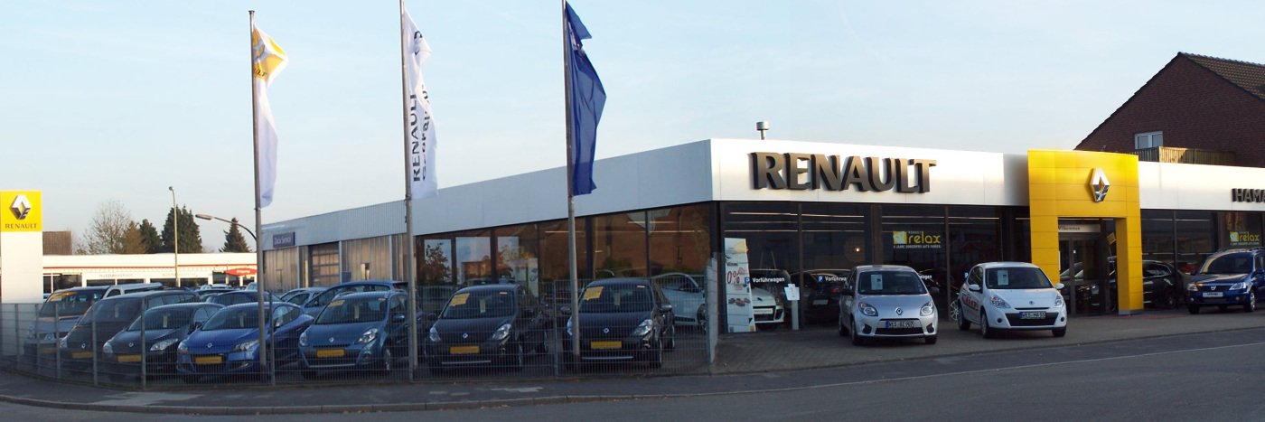 Renault Autohaus mit mehreren Autos auf dem Parkplatz und Flaggen vor der Fassade, helles Abendlicht.