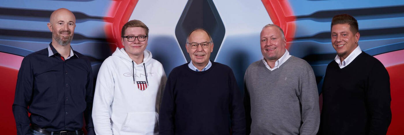 Fünf Personen stehen vor einem grafischen Hintergrund bei einer Veranstaltung. Professionelles Gruppenfoto.