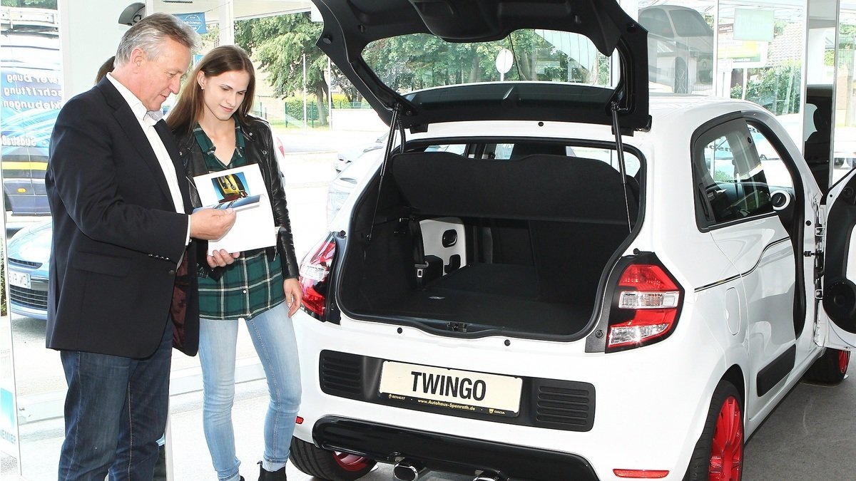 Zwei Personen besichtigen den Kofferraum eines weißen Twingo in einem Autohaus.