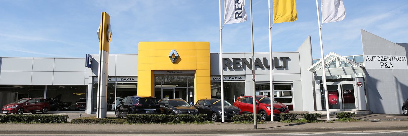 Renault Autozentrum P&A mit Dacia Modellen und Fahnen vor einem modernen Ausstellungsgebäude.
