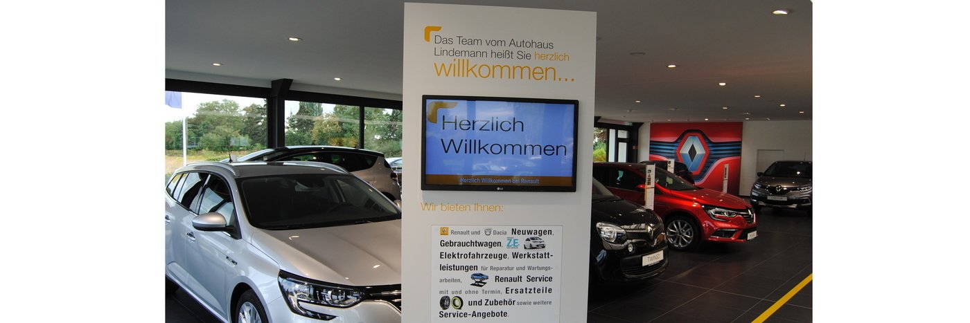 Willkommensschild im Autohaus Lindner mit Autos im Showroom und moderner Einrichtung.