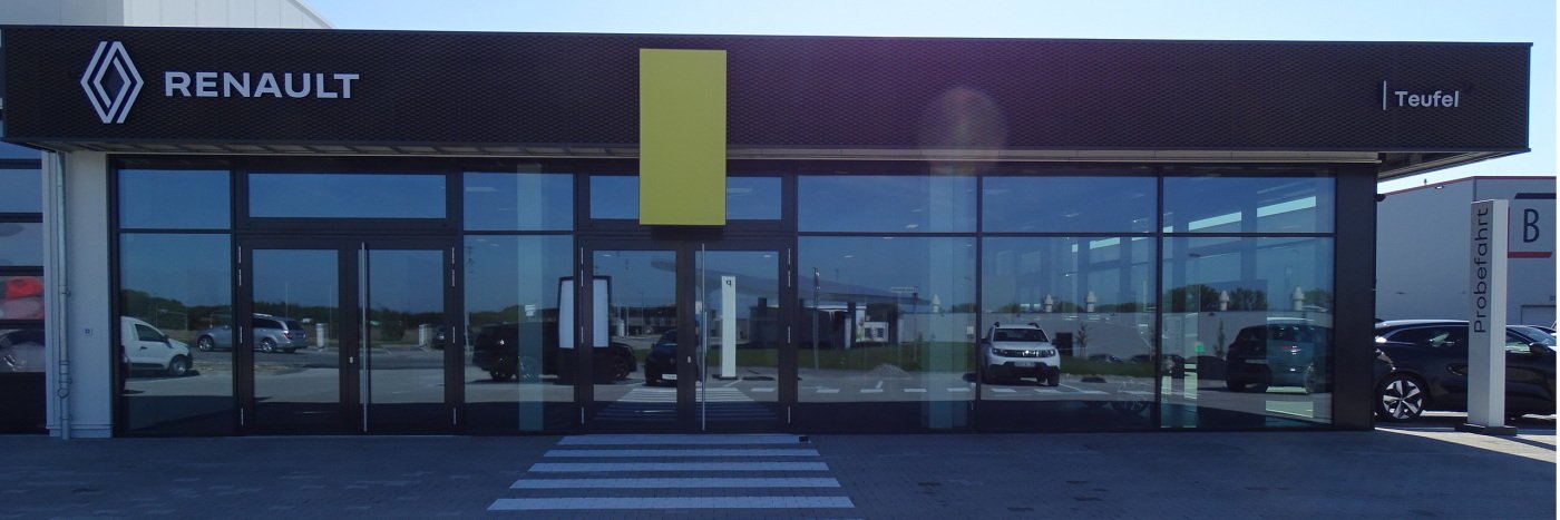 Renault Autohaus Teufel mit großen Glasfenstern und einem gelben Schild, am Parkplatz mit Autos.