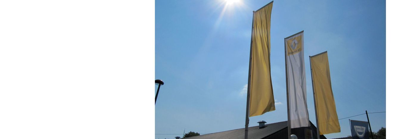 Drei große Fahnen in Gelb und Weiß wehen vor einem Gebäude unter einem klaren blauen Himmel.