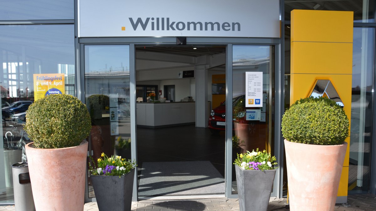 Eingang zu einem Geschäft mit dem Schriftzug 'Willkommen', begrüßt von Pflanzen in dekorativen Töpfen.